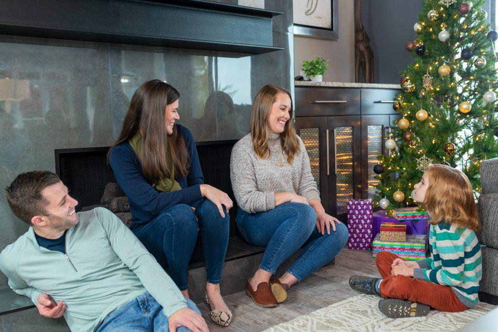 three adults smile and laugh with a child in front of a Christmas tree in a StayLakeNorman luxury vacation rental