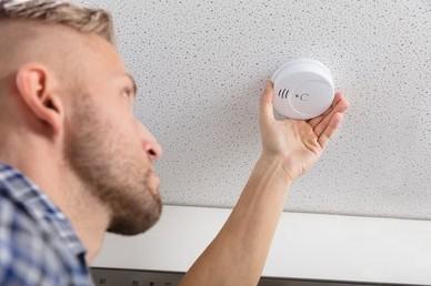 Low angle view of a white male testing a smoke detector in a vacation rental home.