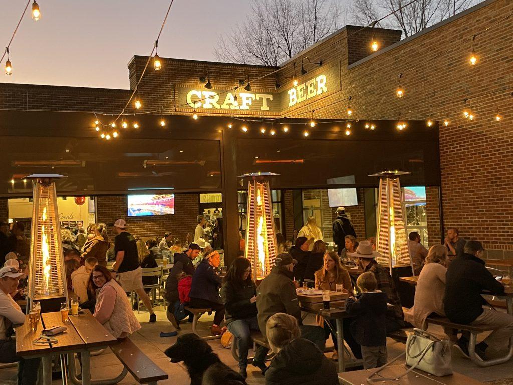 People drinking Hoptown Brewing craft beer on a busy outdoor patio at dusk.