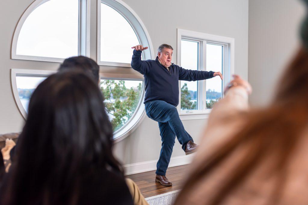 Man playing charades during a company retreat team building activity at a StayLakeNorman luxury vacation rental. 