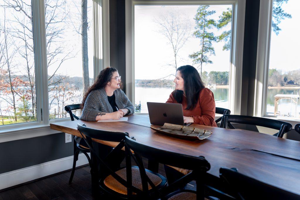 Two women in a breakout session sitting at a table with a waterfront view. 